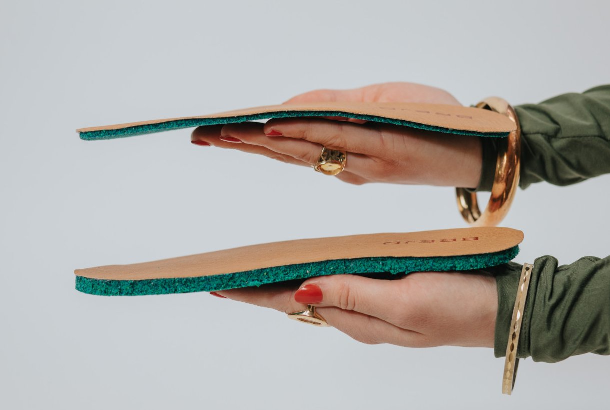 Two leather insoles with green cushioning, held in hands.